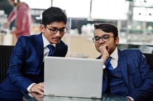 deux hommes d'affaires indiens en costumes assis au bureau sur un café et regardant un ordinateur portable. photo