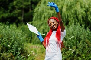 femme bénévole aux cheveux rouge africaine avec presse-papiers dans le parc. concept de volontariat, de charité, de personnes et d'écologie en afrique. photo