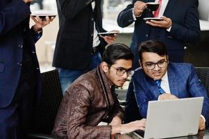 groupe de cinq hommes d'affaires indiens en costumes assis au bureau sur un café regardant un ordinateur portable et buvant du café. photo