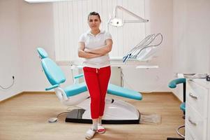 portrait d'une femme dentiste femme bras croisés debout dans son cabinet de dentisterie près de la chaise. photo