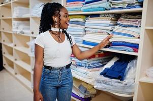 une femme afro-américaine joyeuse se tient près des étagères avec des serviettes dans la blanchisserie en libre-service. photo