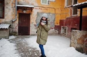 portrait de jeune fille brune en écharpe et chapeau gris, lunettes par temps froid contre le mur orange de la vieille maison. photo