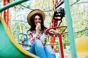 portrait de jeune fille brune à lunettes roses et chapeau avec crème glacée au parc d'attractions. photo