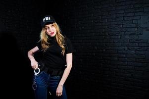 agent féminin du fbi en casquette et avec arme à feu au studio contre un mur de briques sombres. photo