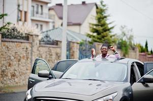 riche femme africaine d'affaires en voiture suv argentée sur le toit ouvrant s'amusant avec de la bière à portée de main. photo