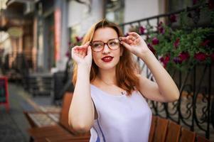 jolie femme rousse à lunettes posant dans la rue de la ville de printemps. photo