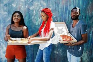 trois joyeux amis afro-américains tenant des boîtes à pizza contre le mur de peinture. photo