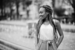 fille afro-américaine à la mode au pantalon rose et aux dreads rouges posées en plein air contre les fontaines. photo