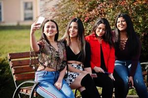 groupe de quatre filles latinos heureuses et jolies de l'équateur posées dans la rue et faisant du selfie au téléphone. photo