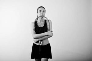 portrait noir et blanc de la belle jeune femme joueuse en vêtements de sport tenant une raquette de tennis en se tenant debout sur fond blanc. photo