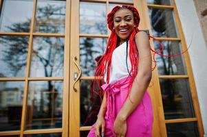 fille afro-américaine à la mode au pantalon rose et aux dreads rouges posées à l'extérieur. photo