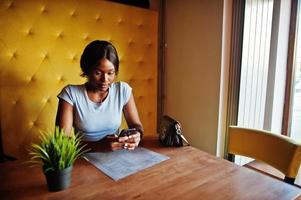 fille afro-américaine assise au café avec téléphone portable. femme noire se reposant. photo