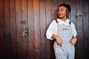 femme afro-américaine en salopette et béret contre un mur en bois. photo