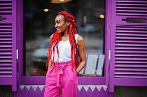 fille afro-américaine à la mode au pantalon rose et aux dreads rouges posées à l'extérieur. photo