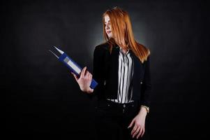 portrait d'une femme d'affaires rousse portant un chemisier rayé, des lunettes et une veste avec un dossier bleu. photo