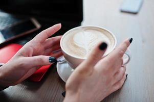 gros plan sur les mains d'une fille avec une tasse de cappuccino sur fond rouge ordinateur portable et téléphone portable. photo