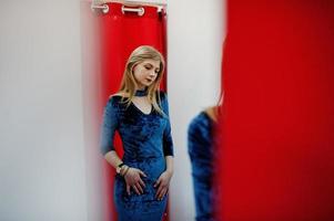 fille blonde en robe bleue dans le magasin de vêtements avec des rideaux rouges. photo