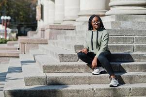 portrait de la ville d'une jeune femme positive à la peau foncée portant un sweat à capuche vert et des lunettes. photo