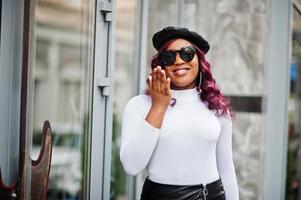 big mama modèle afro-américain taille plus en lunettes de soleil noires, béret et jupe en cuir posés à l'extérieur et envoyer un baiser aérien. photo