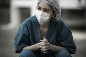 une infirmière asiatique fatiguée et déprimée porte un masque facial uniforme bleu assis sur le sol de l'hôpital, jeune femme médecin stressée par un travail acharné photo