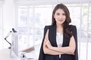une femme de travail asiatique confiante qui a les cheveux longs avec un costume noir est debout et croise les bras dans le concept de travail à domicile. photo