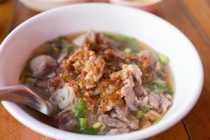 vermicelles de riz nouilles de riz avec soupe de porc contient des boulettes de viande, de la viande et du piment mariné versé sur le dessus sur fond boisé. photo