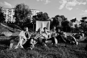 jeune groupe multiethnique de personnes regardant un film au pouf dans un cinéma en plein air. photo