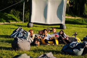 jeune groupe multiethnique de personnes regardant un film au pouf dans un cinéma en plein air. photo