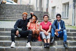 quatre amis africains s'amusant à l'extérieur. deux filles noires avec des gars sont assises dans les escaliers d'une vieille ville. photo
