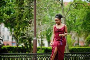 portrait d'une belle jeune femme africaine naturelle aux cheveux afro. modèle noir en robe de soie rouge avec téléphone portable. photo