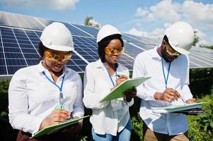 un technicien afro-américain vérifie l'entretien des panneaux solaires. groupe de trois ingénieurs noirs réunis à la station solaire. photo