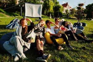jeune groupe multiethnique de personnes regardant un film au pouf dans un cinéma en plein air. photo