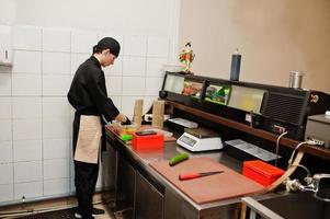 chef professionnel porter en noir faisant des sushis et des petits pains dans une cuisine de restaurant de cuisine traditionnelle japonaise. photo