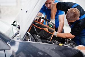 thème de la réparation et de l'entretien des voitures. deux mécaniciens en uniforme travaillant dans le service automobile, vérifiant le moteur. photo