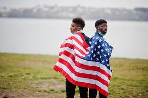 deux adolescents africains amis avec le drapeau américain au parc portant des masques médicaux protègent contre les infections et les maladies coronavirus virus quarantaine. photo
