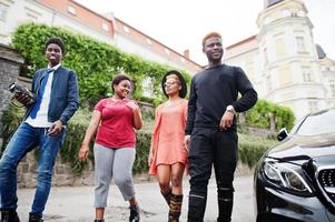 quatre amis africains marchant près d'une voiture de luxe à l'extérieur. deux filles noires avec des gars. photo