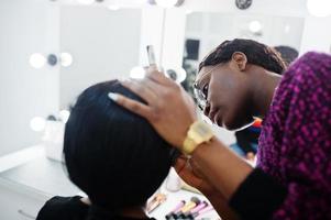 femme afro-américaine se maquillant par une maquilleuse au salon de beauté. photo