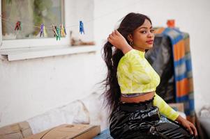 portrait d'une belle jeune femme mannequin afro-américaine, vêtue d'un haut vert et d'un pantalon noir brillant à l'aspect mouillé. photo