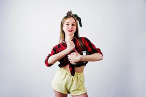 jeune femme au foyer drôle en chemise à carreaux et short jaune pin up style avec casserole et cuillère de cuisine isolé sur fond blanc. photo