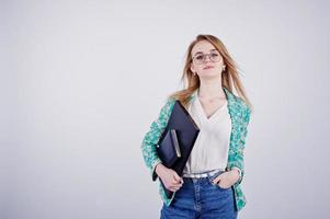 fille blonde élégante en veste et jeans à lunettes avec carnet de notes et ordinateur portable à mains sur fond blanc sur studio. photo