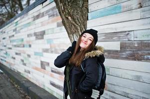 jeune fille porte un couvre-chef noir contre un mur en bois. photo