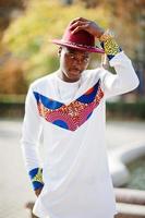 homme afro france élégant et branché en chapeau rouge et tenue blanche posée au jour de l'automne. gars modèle africain noir. photo