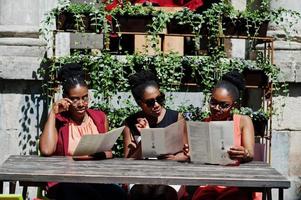 trois élégantes femmes afro-américaines posées à la journée d'été ensoleillée en plein air, assis sur la table du restaurant avec menu à portée de main. photo