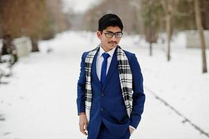 homme étudiant indien élégant en costume, lunettes et écharpe posé à la journée d'hiver en plein air. photo