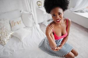 jolie femme afro-américaine aux cheveux afro portant une jupe rose, posée dans la salle blanche. modèle noir sexy à la mode. photo