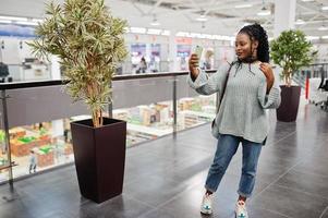 blogueuse africaine posée en pull et jeans posés au centre commercial avec son téléphone portable. photo