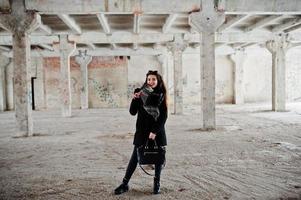 brune élégante fille décontractée en écharpe et sac à main contre la place de l'usine abandonnée. photo