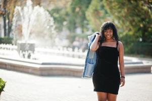 femme bouclée afro france élégante et branchée posée au jour de l'automne en veste de jeans. modèle féminin africain noir contre la fontaine. photo