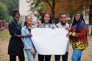 un groupe de cinq étudiants africains sur le campus de la cour de l'université tient un blanc vide. espace libre pour votre texte. amis afro noirs qui étudient. photo