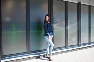 portrait de jeune fille brune en chemise à carreaux bleu contre de grandes fenêtres. photo